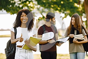 Three international students standing in a park and holding a books