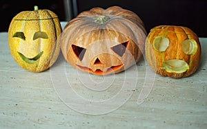 Three jack-o`-lanterns from pumpkin and melons on kitchen table.