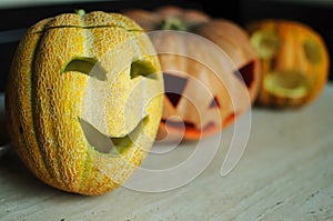 Three jack-o`-lanterns from pumpkin and melons on kitchen table.