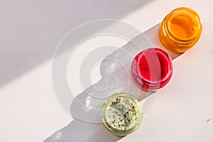 Three jars of colorful jams and honey on white