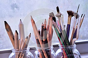 Three jars with fine art tools. Paintbrushes, pencils and tortillons.