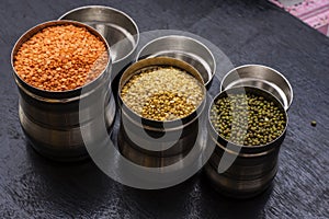 Three jars full of mung dal, green mung and munsuri dal three types of lintel on a black wooden table