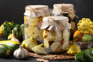 Three jars with pickled patissons, cucumbers and zucchini on dark gray background with fresh ingredients, Horizontal