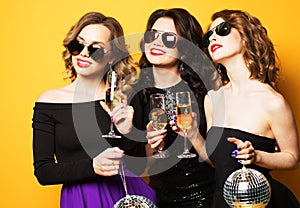 Three joyful charming young women friends with disco balls drinking champagne