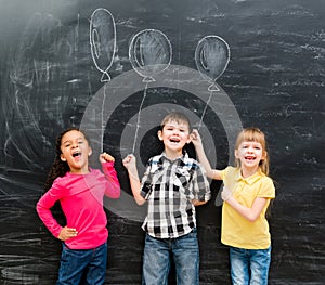 Three joyful children keep imaginary balloons drawn on the blackboard