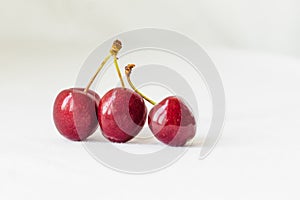 Three juicy berries of a red cherry on a white fabric background