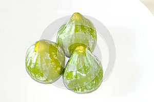 Three organic fresh green figs, on white background, from above