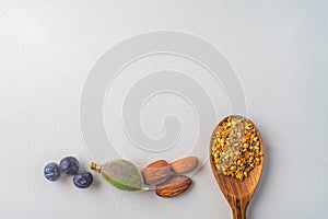 Three juniper blue old berries, almonds nut and bee pollen in wooden spoon on spring, isolated on white textured paper. Copy space