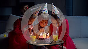 Three kids in birthday hats drinking fruit juice with straw at home. Brother and sisters celebrate birthday with