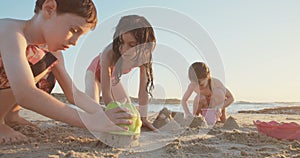 Three kids building sand castles on the beach during sunset