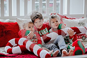 Three kids in Christmas pyjamas laying on white big bed with Christmas pillows