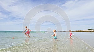 Three kids, little boys and girl play with ball at ocean beach