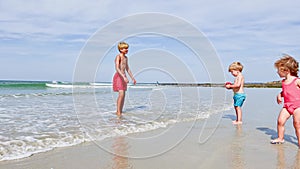 Three kids, little boys and girl play with ball in sea at beach