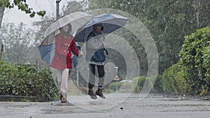 Three kids running happy in the rain and puddles with umbrellas