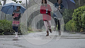 Three kids running happy in the rain and puddles with umbrellas