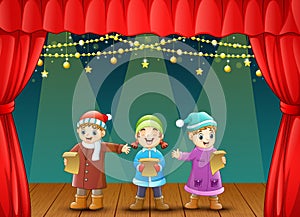 Three kids singing christmas carols on stage