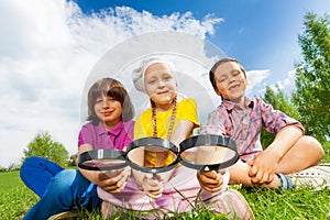 Three kids sitting close together with magnifiers