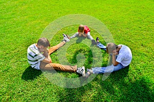 Three kids are sitting on green grass holding hands in a park
