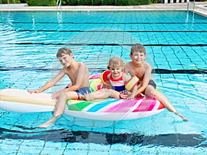 Three kids, two boys and toddler girl splash in an outdoors swimming pool in summer. Happy children, brothers and sister