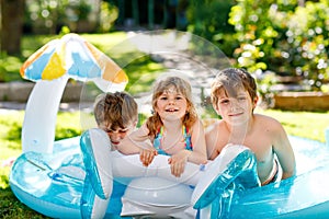 Three kids, two boys and toddler girl splash in an outdoors swimming pool in summer. Happy children, brothers and sister