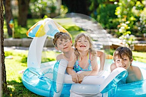 Three kids, two boys and toddler girl splash in an outdoors swimming pool in summer. Happy children, brothers and sister