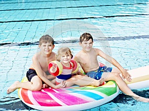 Three kids, two boys and toddler girl splash in an outdoors swimming pool in summer. Happy children, brothers and sister