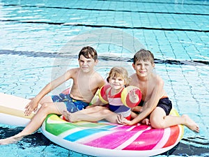 Three kids, two boys and toddler girl splash in an outdoors swimming pool in summer. Happy children, brothers and sister