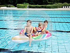Three kids, two boys and toddler girl splash in an outdoors swimming pool in summer. Happy children, brothers and sister
