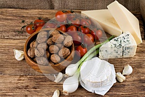 Three kinds of cheese and various vegetable on wooden board