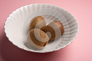 Three kiwis on bowl over pink background