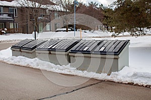 Three large metal garbage bin sits on the side of a street in a condo corporation