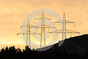 Three large overland electricity pylons in the morning light in the mountains.