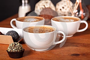 Three latte cups and small cakes on the wooden table in the cafe. Communication over a Cup of coffee, Coffee break