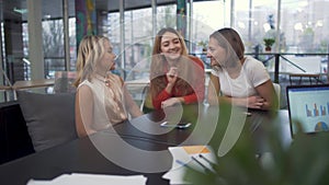 Three laughing joking girls sitting at boardroom table during a break in a business meeting.