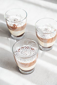Three-layer chocolate and vanilla mousse dessert in glass cups, sprinkled with coconut flakes, on a children's