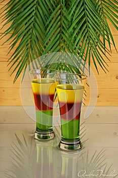 Three-layer cocktail on a mirrored table and palm tree background.