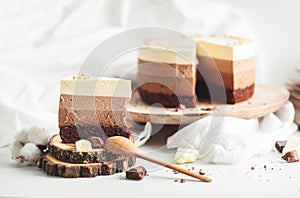 Three layered chocolate mousse cake on the wooden stand on white background. Good morning with fresh coffee and chocolate souffle