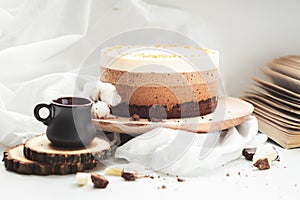Three layered chocolate mousse cake on the wooden stand on white background. Good morning with fresh coffee and chocolate souffle