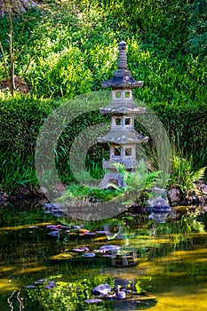 Three level stone lantern sits on a small island in a clear pond surrounded by lush green