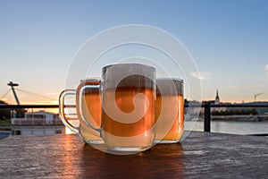 Three light beer glasses on the wooden table on background sky and sunset