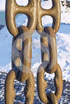 Three links of iron chains in the seaport hang against the background of snow