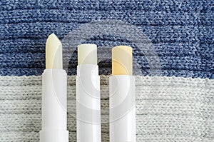 Three lip balms on the knitted background. Winter lip care sticks with beeswax, honey, panthenol and shea butter. Copy space. photo