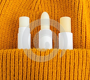 Three lip balms on the orange knitted background pocket. Winter lip care sticks with beeswax, honey, panthenol and shea butter.