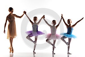 Three little ballerinas dancing with personal ballet teacher in dance studio