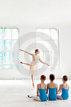 Three little ballerinas dancing with personal ballet teacher in dance studio