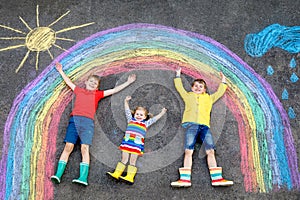 Three little children, two school kids boys and toddler girl having fun with with rainbow picture drawing with colorful