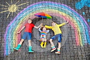 Three little children, two school kids boys and toddler girl having fun with with rainbow picture drawing with colorful