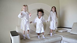 Three little girls are jumping on the couch.