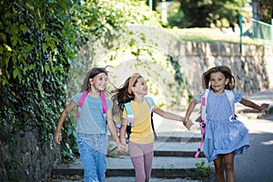 Three little girls running trough park and with school bags