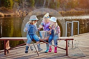 Three little happy girls brag about fish caught on a fishing pole. Fishing from a wooden pontoon.